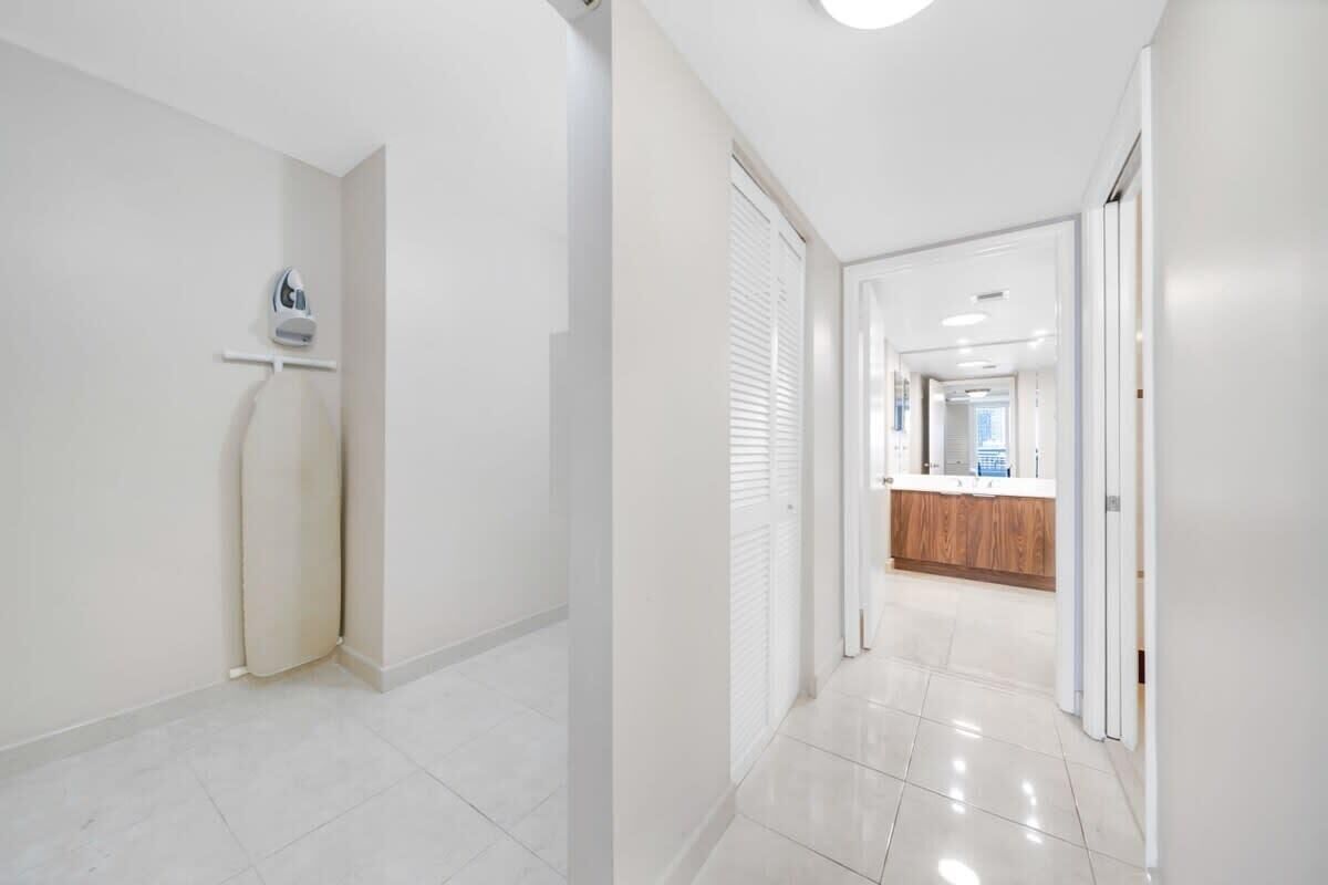 A modern hotel corridor with a clean, white interior, a reception area with a wooden counter, and a visible iron in the corner.