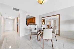 A modern dining area with a round table and chairs, a kitchen visible through an open door, and a large mirror on the wall. - Bay Overlooking Balcony & Full Kitchen | StayCozy (Miami)