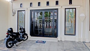 A motorcycle parked outside a building with large glass doors and windows, a tiled floor, and a small rug. - Hotel O Guest House Nusa Indah Syariah (Bandar Lampung)