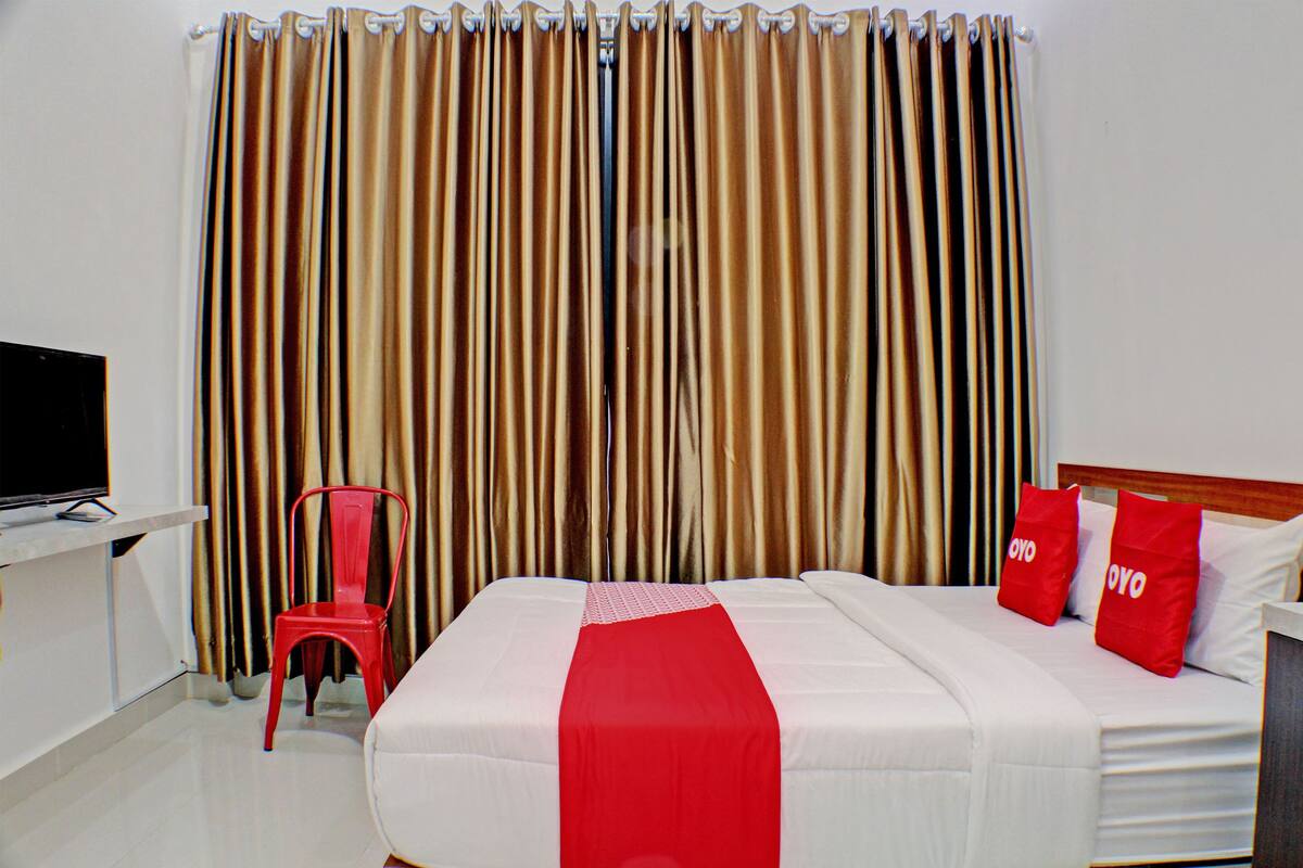 A hotel room with a bed, a TV, a red chair, and curtains.