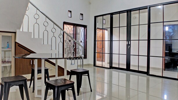 A spacious room with a staircase, a dining area with a table and chairs, and a sliding glass door leading to another room. - Hotel O Guest House Nusa Indah Syariah (Bandar Lampung)