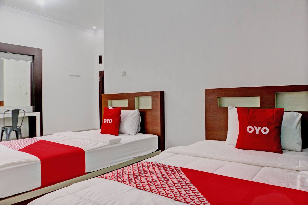 A hotel room with two single beds, each with a red OYO branded pillow, white bedding, and a red and white patterned blanket.