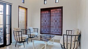 A room with a glass-top table, two chairs with cushions, and a large window with blinds. - Hotel O Guest House Nusa Indah Syariah (Bandar Lampung)