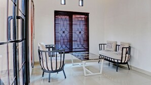 A modern dining area with a glass partition, a black metal table, and two chairs with white cushions. - Hotel O Guest House Nusa Indah Syariah (Bandar Lampung)