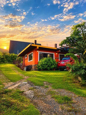 A modern house with a red exterior, a paved driveway, and a red car parked in the driveway.