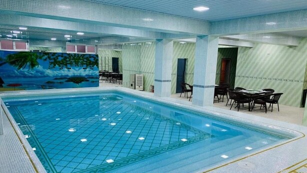 An indoor swimming pool with tiled walls and ceiling, surrounded by seating areas and a mural depicting a tropical scene. - Samarkand (Samarkand)