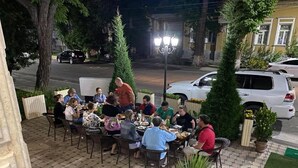 An outdoor dining area with multiple tables and chairs, surrounded by potted plants and a street view. - Samarkand (Samarkand)