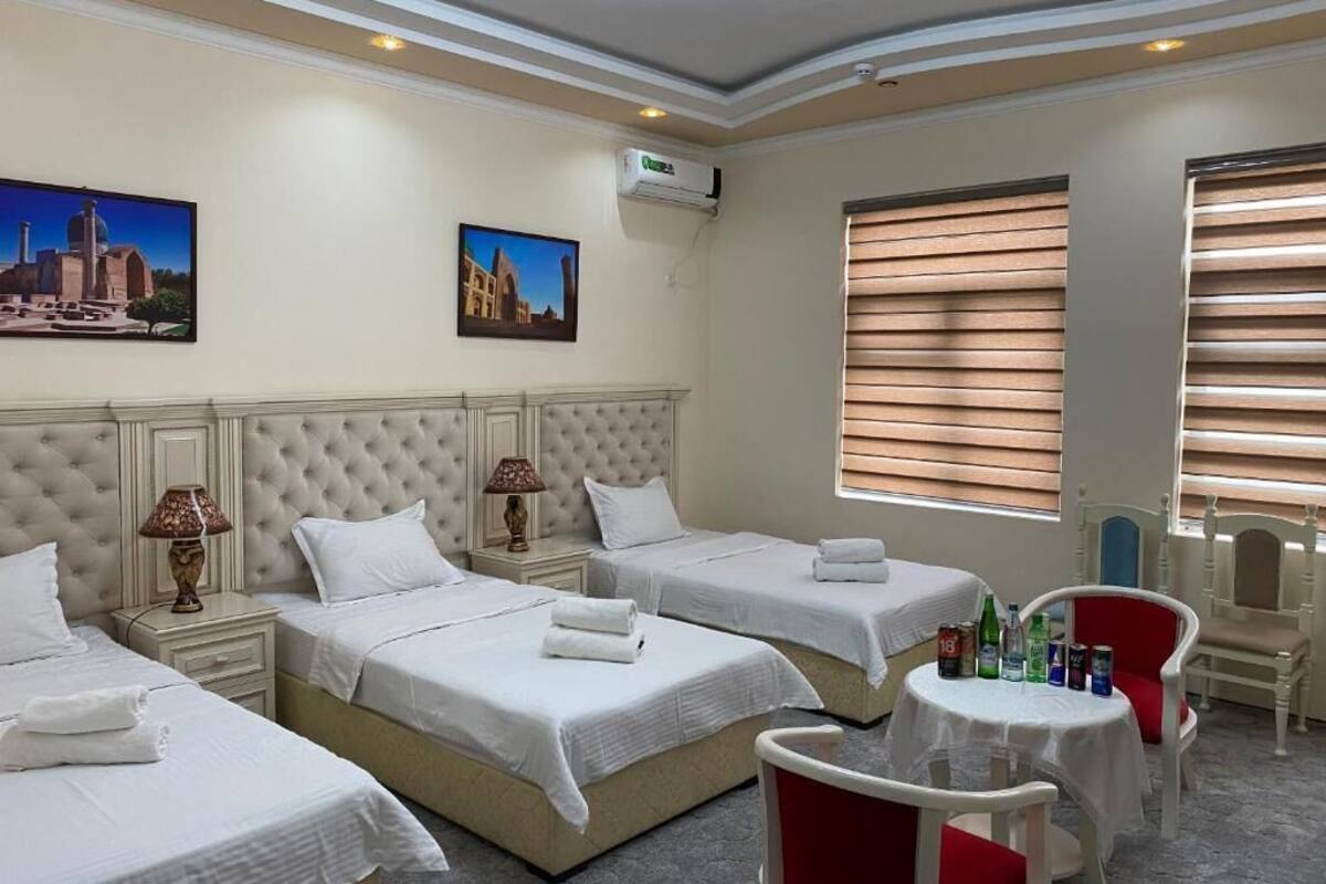 A hotel room with two beds, a small table, a chair, and a window with blinds.