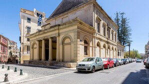 Un edificio histórico con arquitectura clásica, una calle adoquinada y coches estacionados.