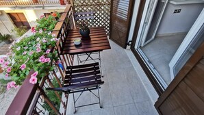 Ein Balkon mit Holztisch und Bänken, umgeben von Blumentöpfen und Blumen.