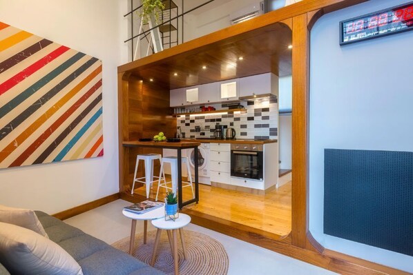 A modern kitchen with a wooden countertop, white cabinets, and a black backsplash. There is a small seating area with stools and a table.