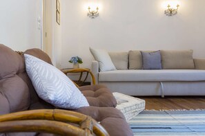 Un salon avec un canapé marron, un canapé blanc et une petite table d’appoint sur laquelle se trouve un vase de fleurs.