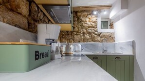 Una cucina con parete in pietra, una cassetta per il pane, una moka e un lavandino.