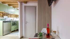 Una stanza compatta con angolo cottura, zona pranzo con tavolo apparecchiato per due e un letto con coperta rosa.