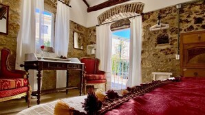 A room with a large bed, a wooden table with a vase, two chairs, and a view of the outside through a window. - The Old Oven House - The apartment was renovated to strict traditional standards. (Corfu)