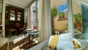 A hotel room with a bed, a dining table with chairs, a glass-top table with drinks, and a view of the outside balcony with potted plants. - The Little Patio House (Corfu)