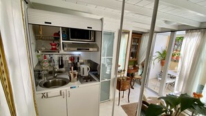 A compact kitchen with a microwave, sink, and various utensils. A dining area with a table and chairs is visible through an open door. - The Little Patio House (Corfu)