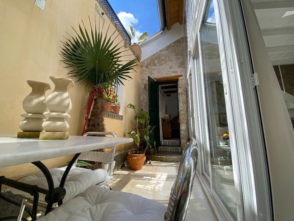 A sunlit patio with a table, potted plants, and a door leading to a room.