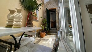 A sunlit patio with a table, potted plants, and a door leading to a room. - The Little Patio House (Corfu)