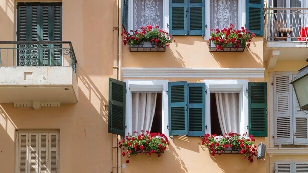 Un edificio de varios pisos con balcones, jardineras y una tienda en la planta baja.
