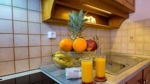 Una encimera de cocina con un bol de frutas que contiene naranjas, una piña y plátanos, junto con dos vasos de jugo de naranja.