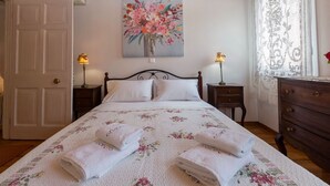 Un dormitorio con una cama, dos mesitas de noche, un aparador y un cuadro en la pared, además de una puerta.