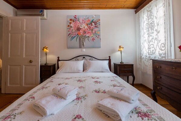 A bedroom with a bed, two bedside tables, a dresser, a painting on the wall, and a door.