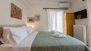 A neatly made bed with white and green linens, a wall-mounted TV, and a radiator. - Pausa Verde - Recently renovated apt, private parking (Corfu)
