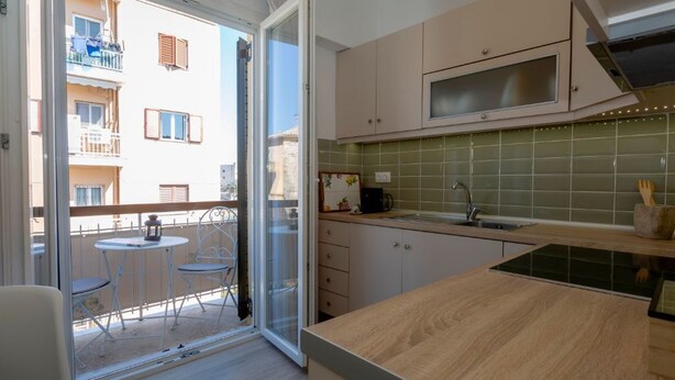 A modern kitchen with a large window, a balcony with chairs, and a view of a building. - Le Boulevard - stylish, renovated apartment (Corfu)