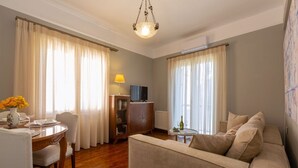 A living room with a sofa, a dining table with chairs, a TV, and a lamp. - Le Boulevard - stylish, renovated apartment (Corfu)