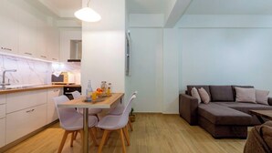 Een moderne keuken met witte kasten, een houten eettafel en een bruine bank in de woonkamer.