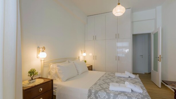 Een slaapkamer met een bed, nachtkastjes, een kledingkast en een deur naar een andere kamer.