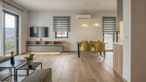 Ein modernes Wohnzimmer mit Essbereich, einem flachbildfernseher an der Wand und einem Balkon mit Blick.