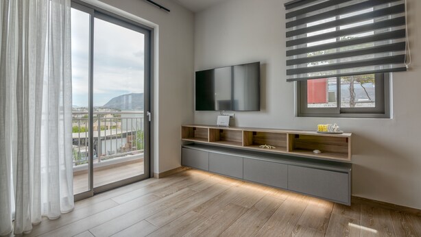 Ein modernes Wohnzimmer mit einer großen Glasschiebetür, die auf einen Balkon führt, einem Wand-Fernseher und einer eingebauten Unterhaltungseinheit mit Regalen.