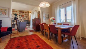 Een eethoek met een houten tafel en rode stoelen, een boekenkast en een rode vloerkleed.