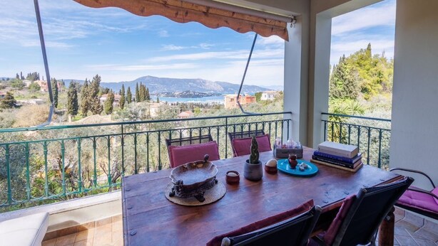 Een balkon met uitzicht op een bergachtig landschap, een houten tafel met een decoratieve schaal en enkele boeken.