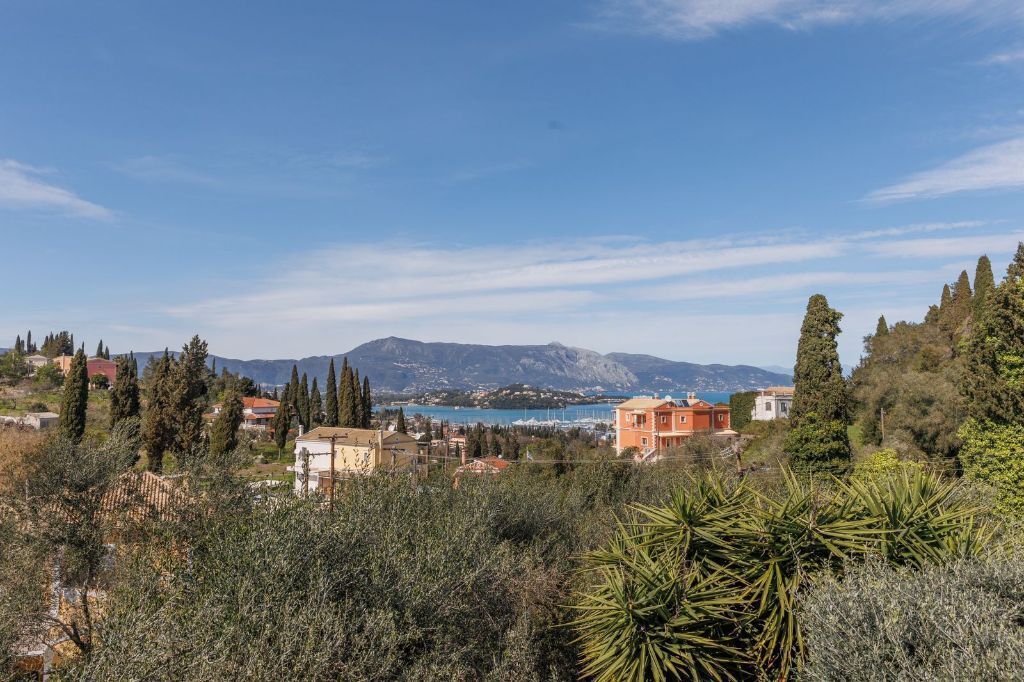 A coastal town with Mediterranean architecture, including terracotta-roofed buildings and cypress trees.