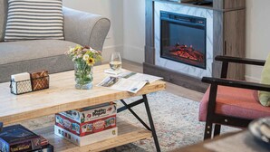 A cozy living room with a fireplace, a coffee table with books and a vase of flowers, and a comfortable sofa. - Revytalize - Cozy 3 Bedroom Condo (Revelstoke)