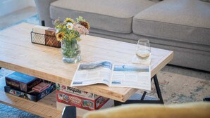 A wooden coffee table with a magazine, a glass of water, and a vase of flowers. - Revytalize - Cozy 3 Bedroom Condo (Revelstoke)