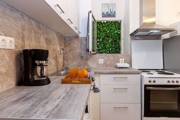 Una cocina moderna con cafetera, bandeja de frutas, estufa y un llamativo panel verde.