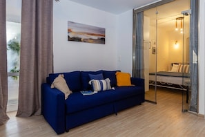Una sala de estar moderna con un sofá azul, un ventanal que da a un dormitorio y un cuadro en la pared.
