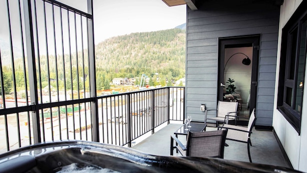 A balcony with a hot tub, outdoor seating, and a view of a forested area. - The Three Bear Penthouse - with Hot Tub (Revelstoke)