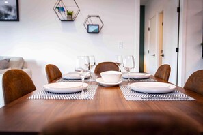 Une table à manger, dressée avec des assiettes, des verres et un saladier, entourée de chaises.