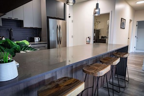 A modern kitchen with a large island, bar stools, and a potted plant. - The Three Bear Penthouse - with Hot Tub (Revelstoke)