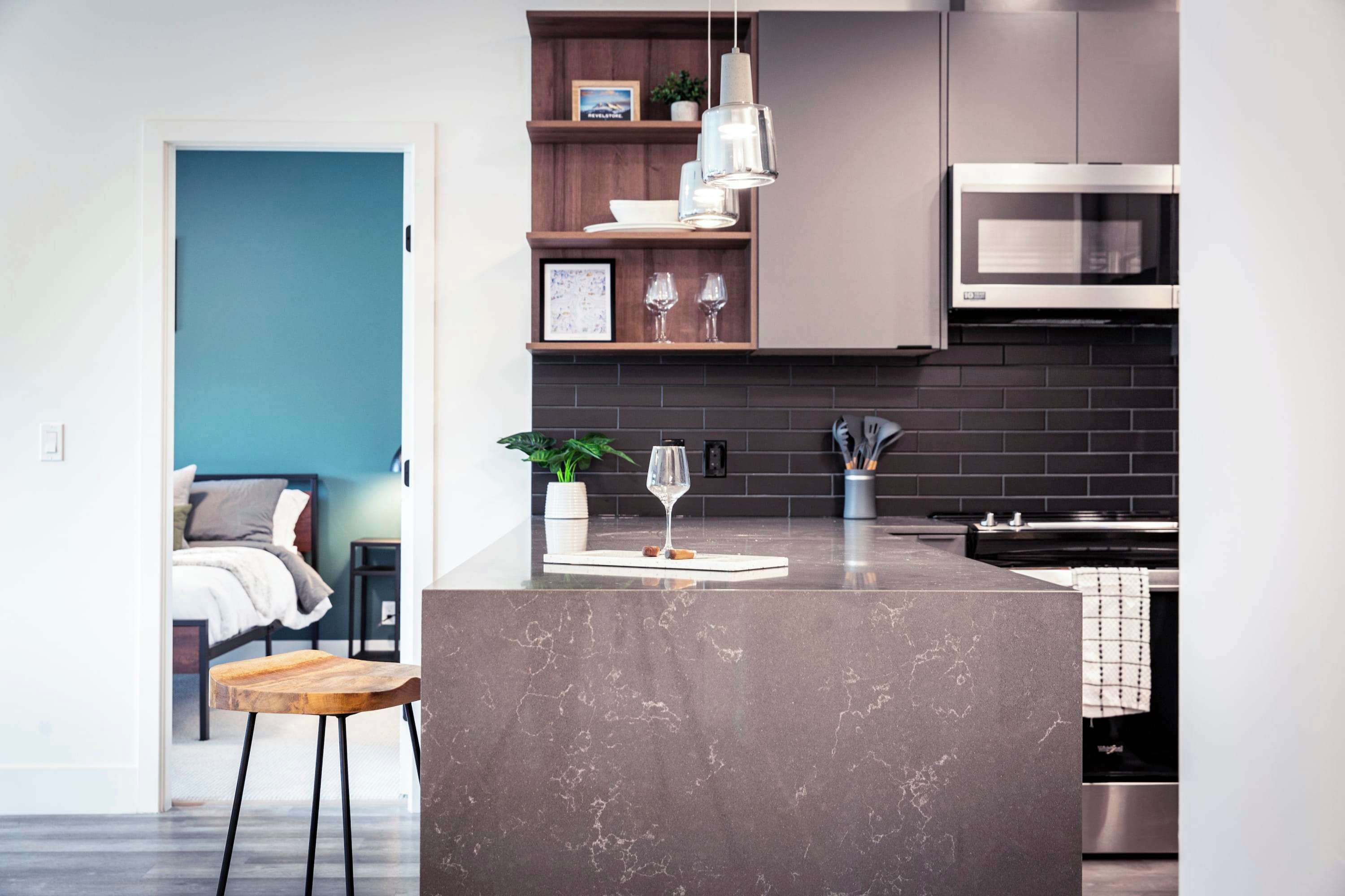 A modern kitchen with a marble island, stainless steel appliances, and a wooden shelf with decorative items.