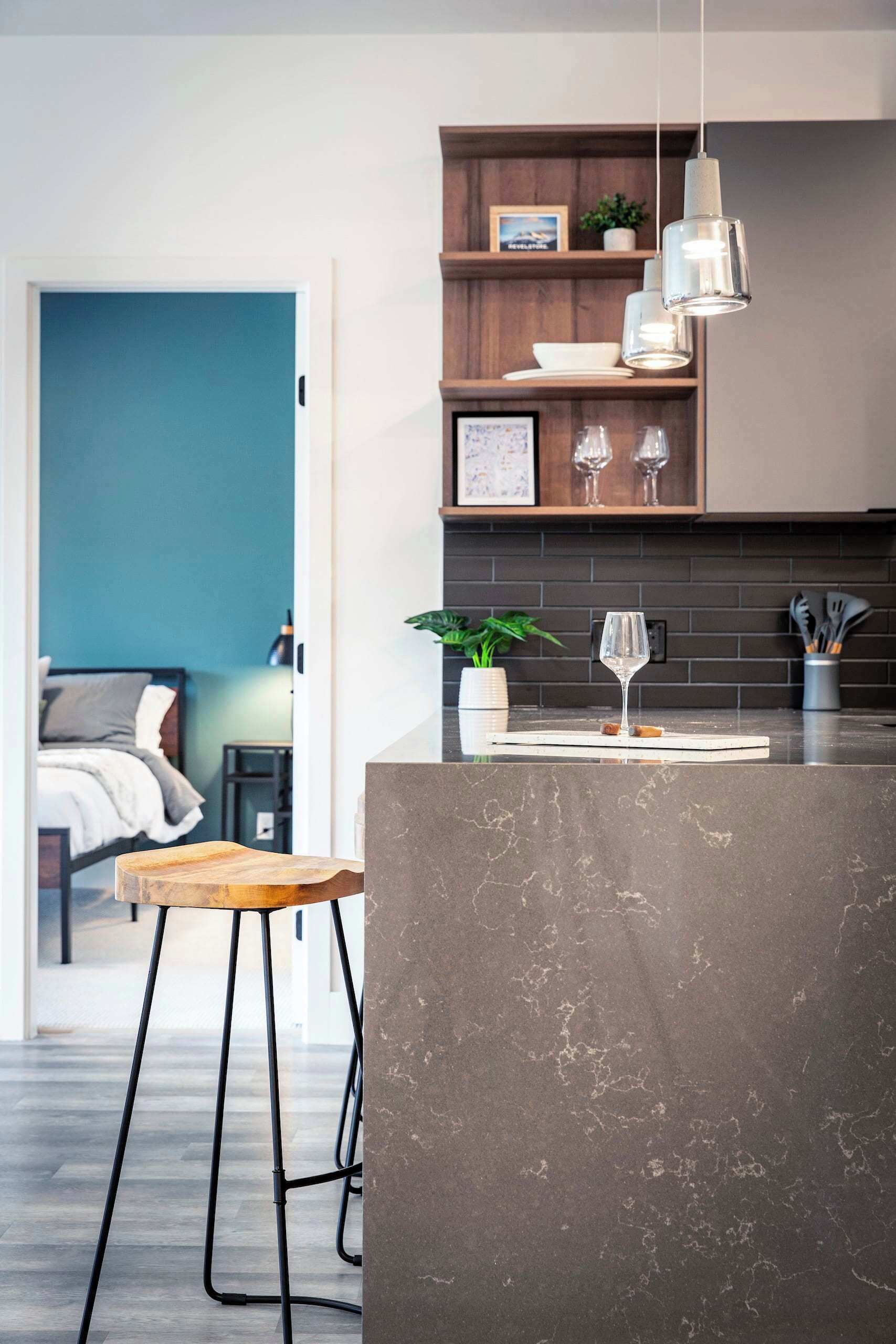 A modern kitchen with a marble countertop, pendant lights, and a wooden stool.