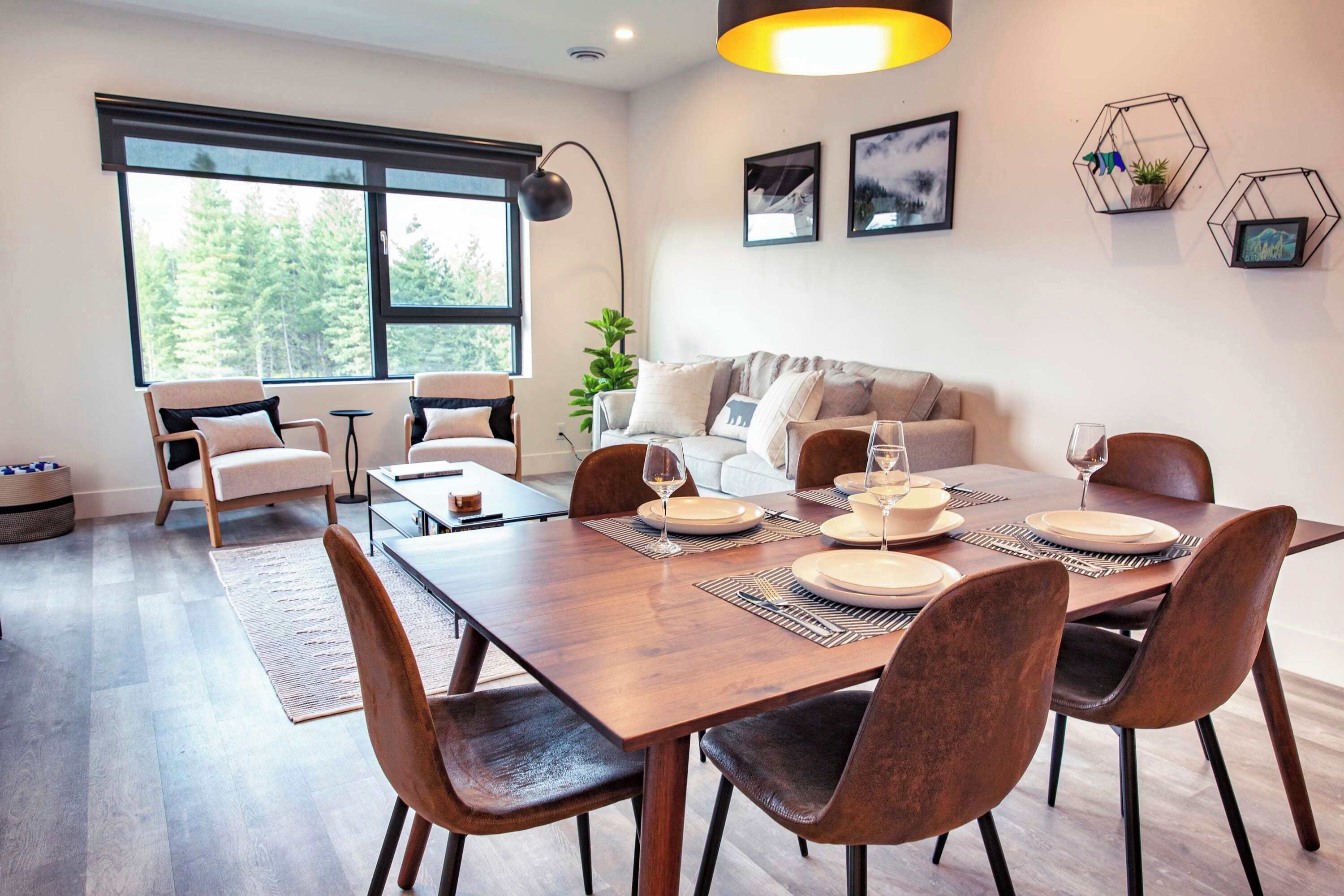 A modern dining area with a wooden table set for six, surrounded by chairs.
