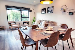 A modern dining area with a wooden table set for six, surrounded by chairs. - The Three Bear Penthouse - with Hot Tub (Revelstoke)
