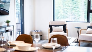 A dining area with a table set for four, a sofa, and a television on the wall. - The Three Bear Penthouse - with Hot Tub (Revelstoke)