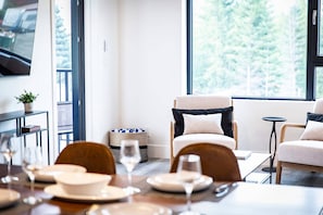 A dining area with a table set for four, a sofa, and a television on the wall. - The Three Bear Penthouse - with Hot Tub (Revelstoke)